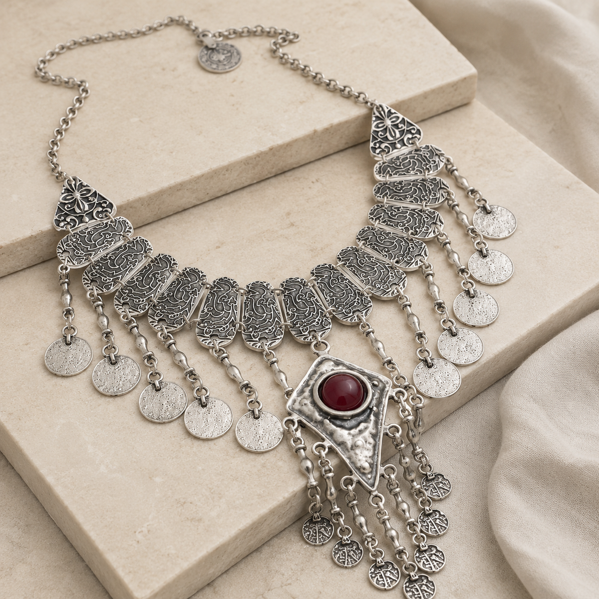 Angled view of a silver-tone coin tassel necklace with textured details.