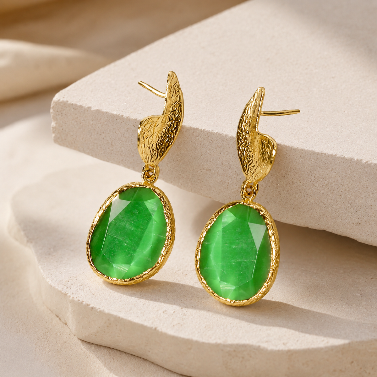 Angled view of long drop earrings with green faceted stones and a gold-plated finish.