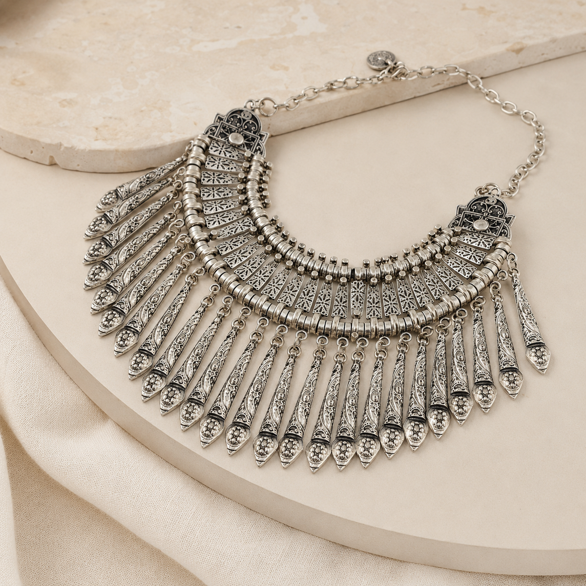 Angled view of the silver-tone collar necklace with layered fringe and textured paddle details.