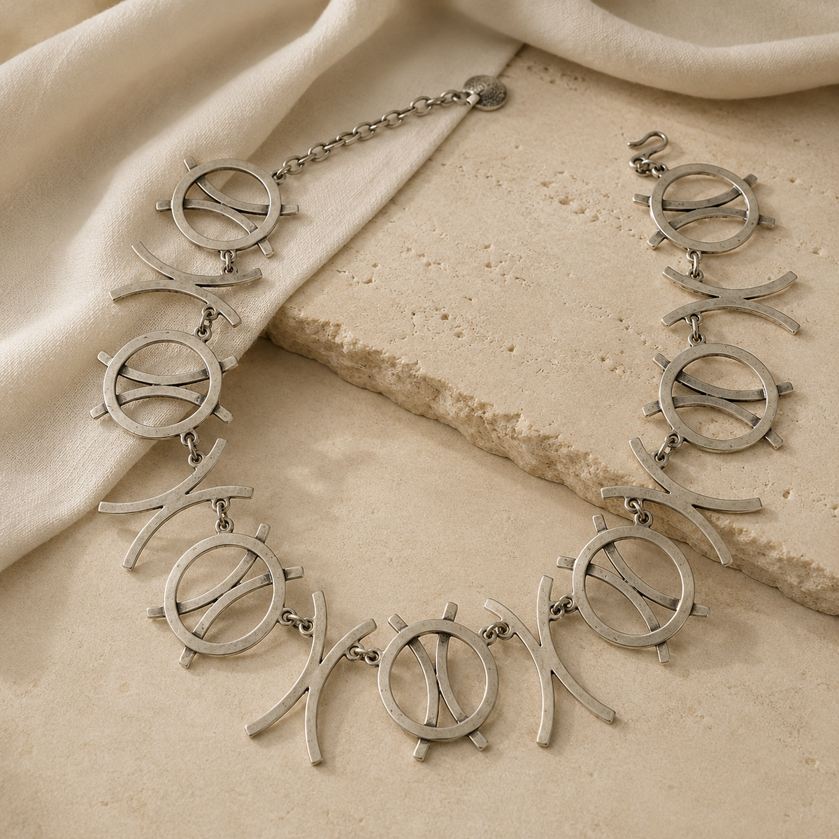 Silver-tone necklace with linked circle symbols and curved shapes shown at an angle.
