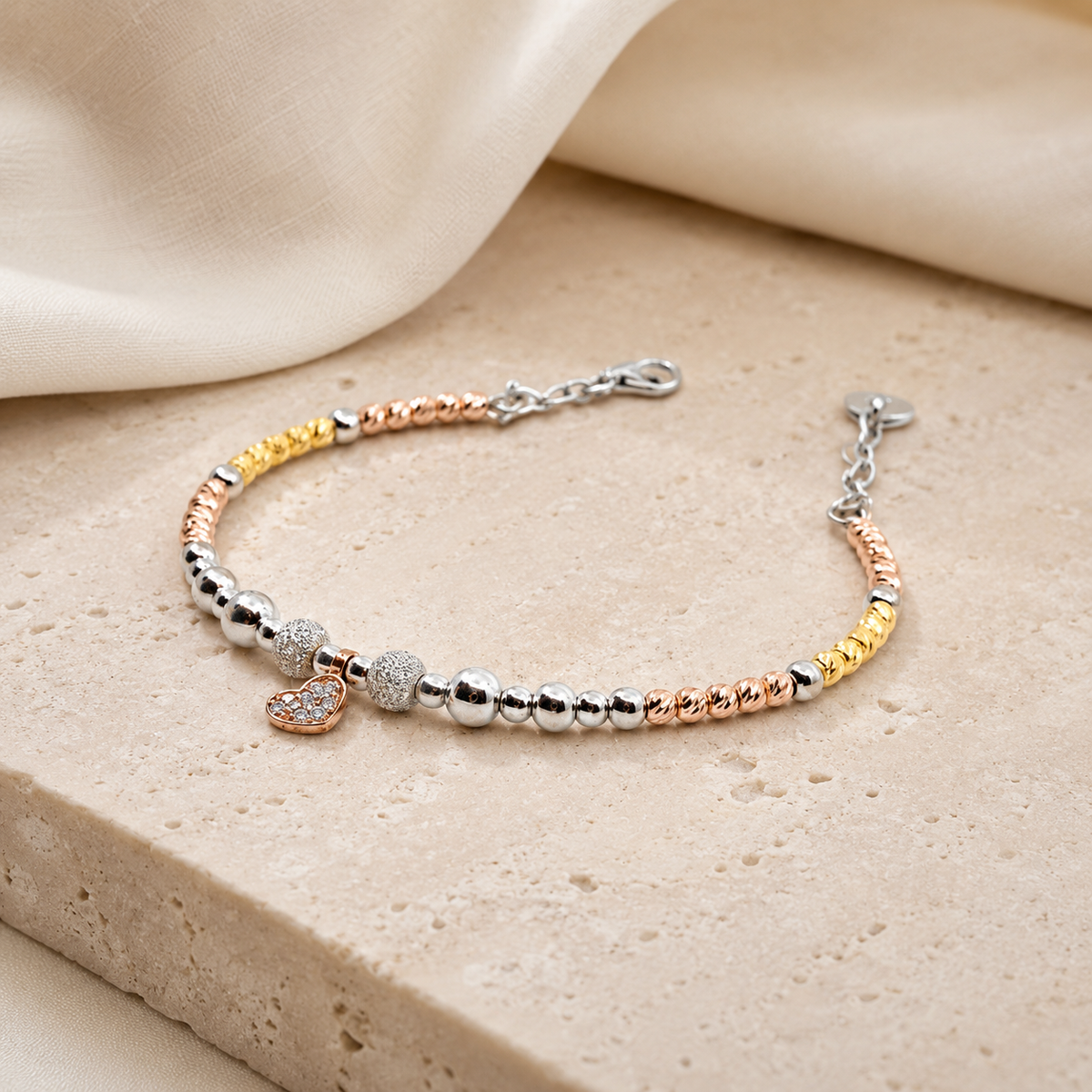 An angled view of a heart bracelet with gold, silver, and rose-toned beads.