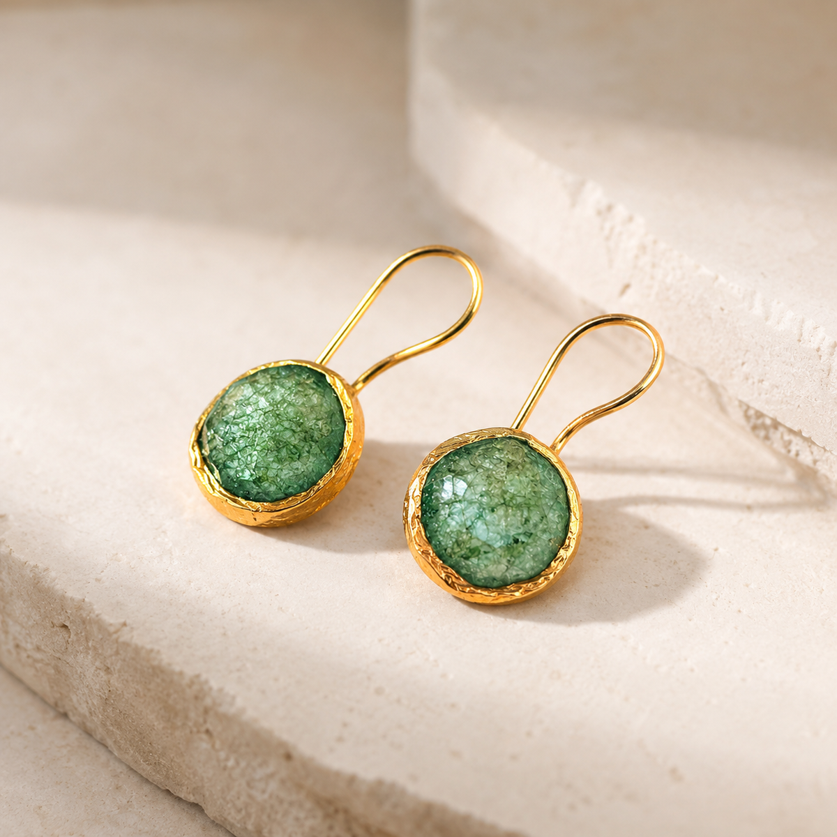Angled view of green stone drop earrings with a polished gold-plated finish.