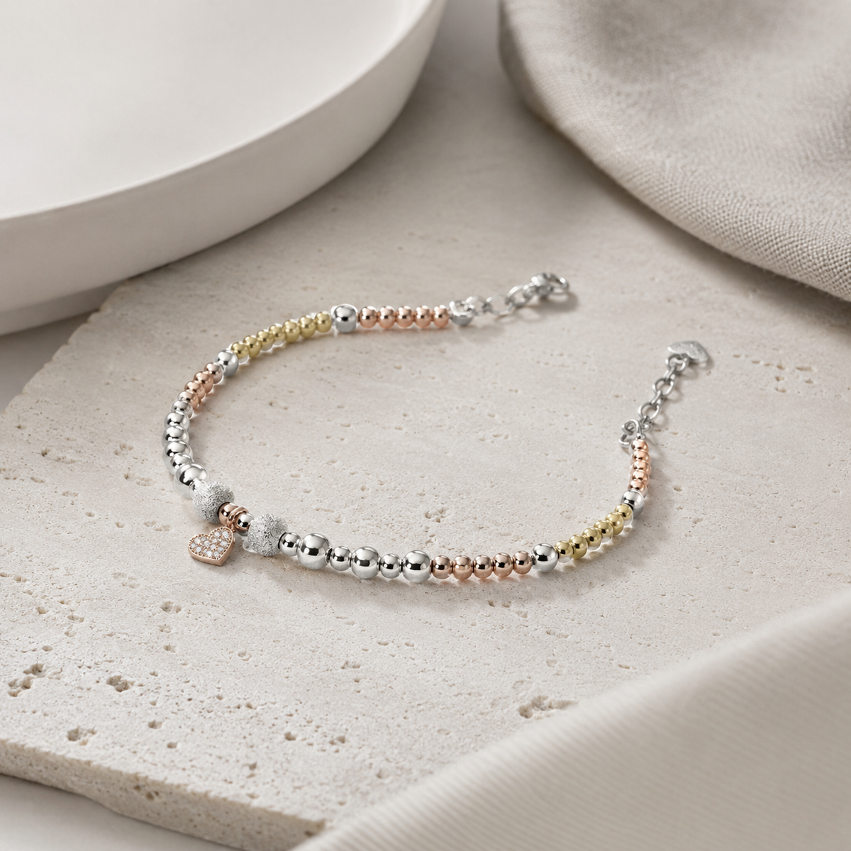 An angled view of the bracelet showing mixed metallic beads and a heart charm.