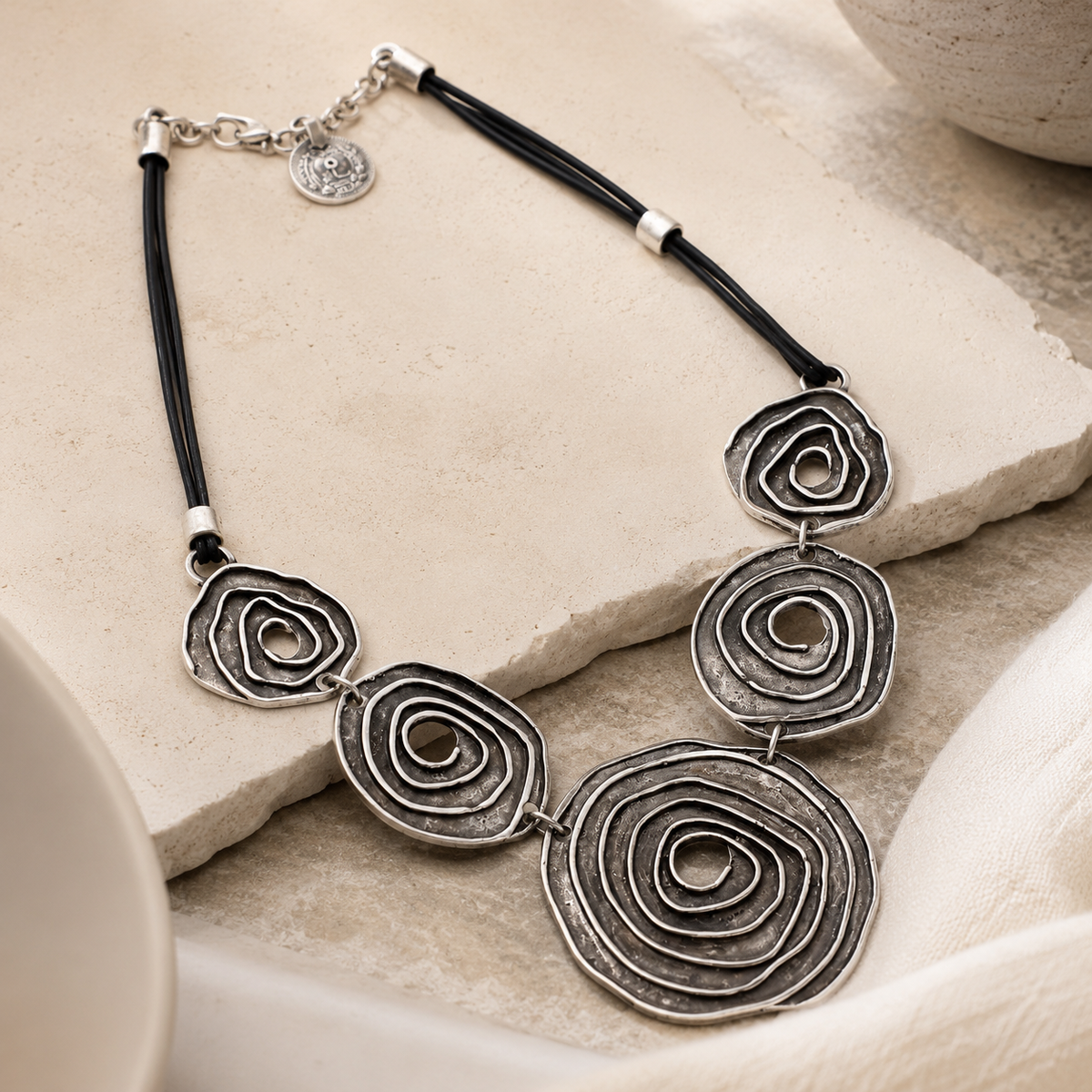 Angled view of a black cord necklace with layered spiral circle pendants.