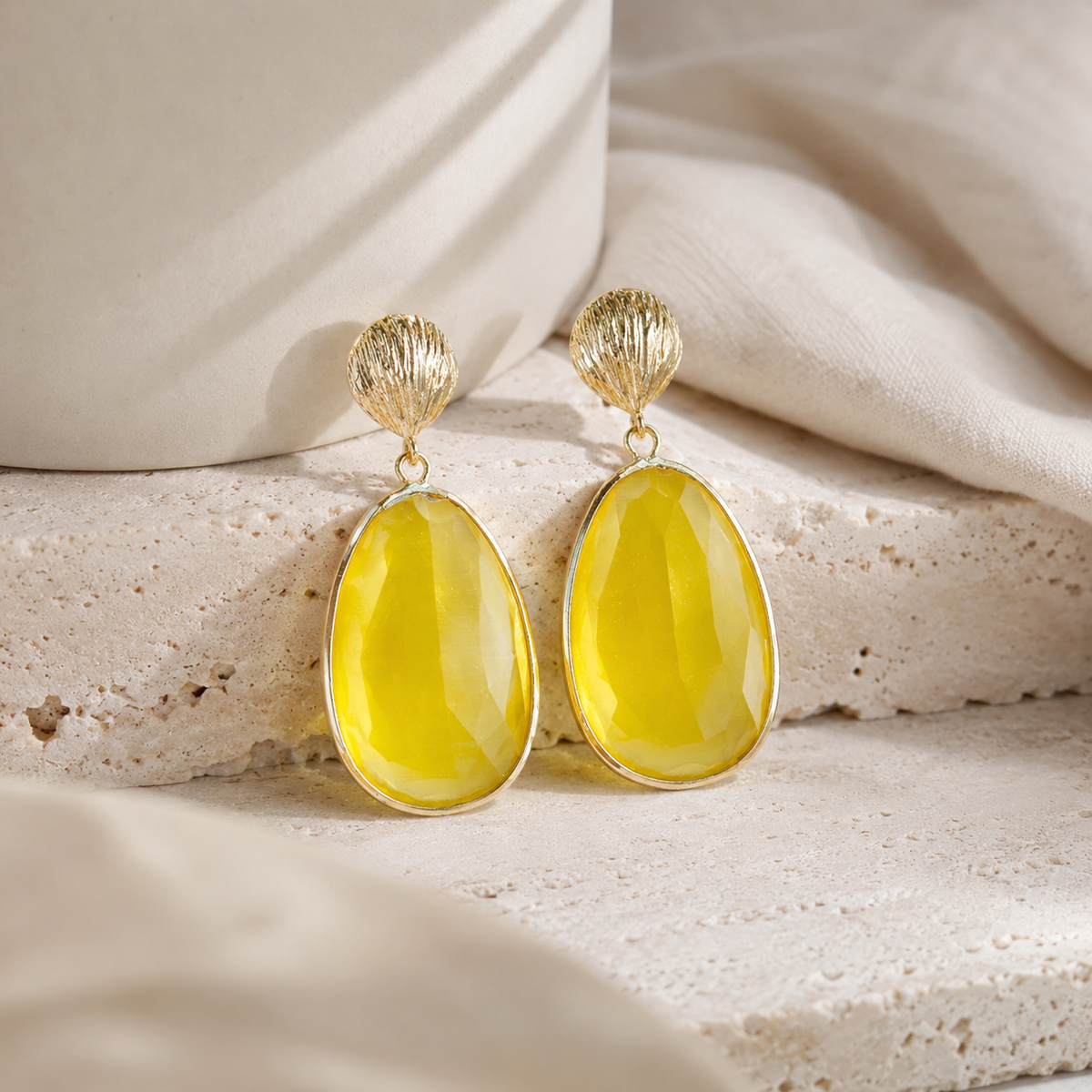 Angle view of gold-tone statement earrings with a textured shell top and faceted yellow cat eye drop.