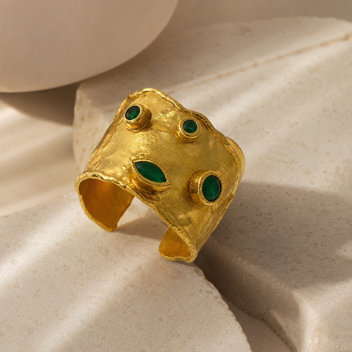 Angled view of a gold-plated cuff ring with emerald green stones and an open adjustable shape.
