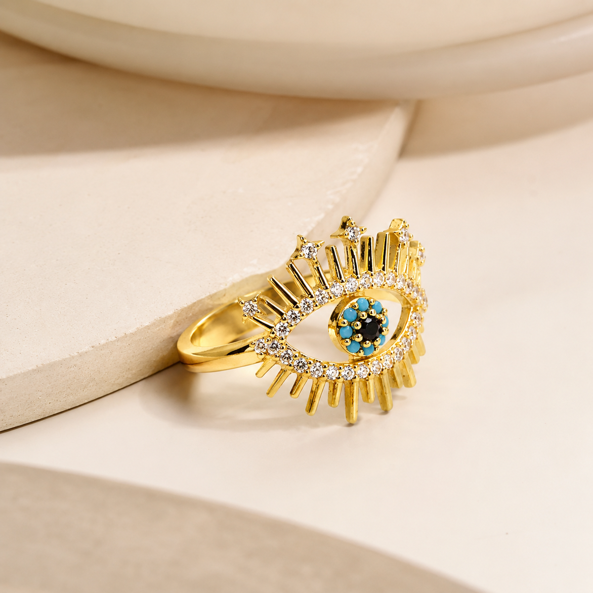 Angled view of a gold-tone evil eye ring with blue and clear crystal-like stones.
