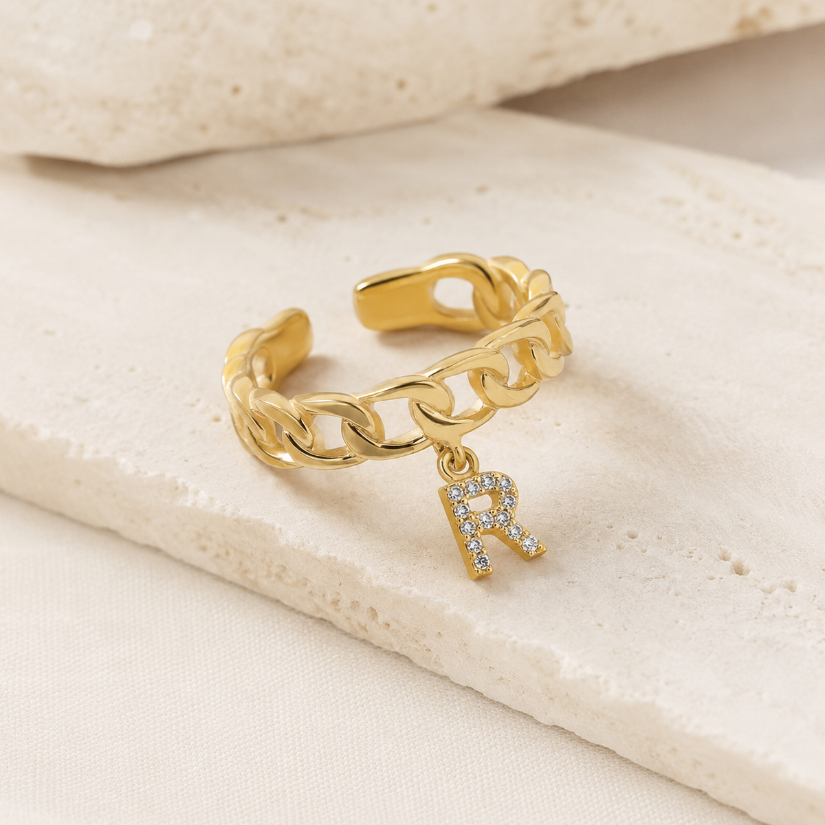 Angled view of a gold-tone chain ring with initial detail.