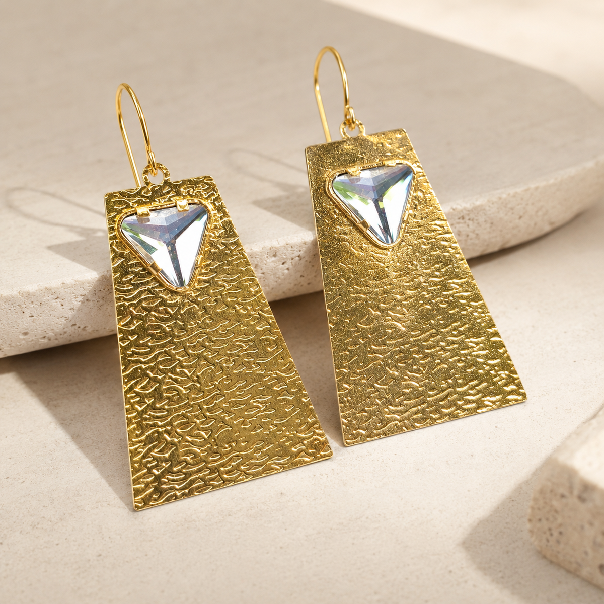 Angle view of textured gold geometric earrings with a clear crystal detail.