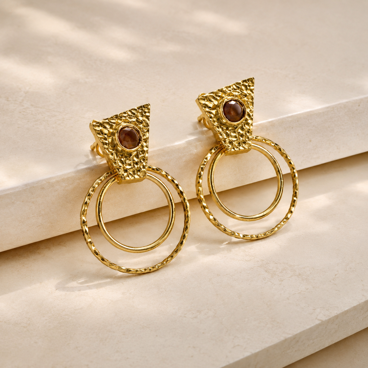 Angle view of textured gold-plated drop earrings with circular shapes.