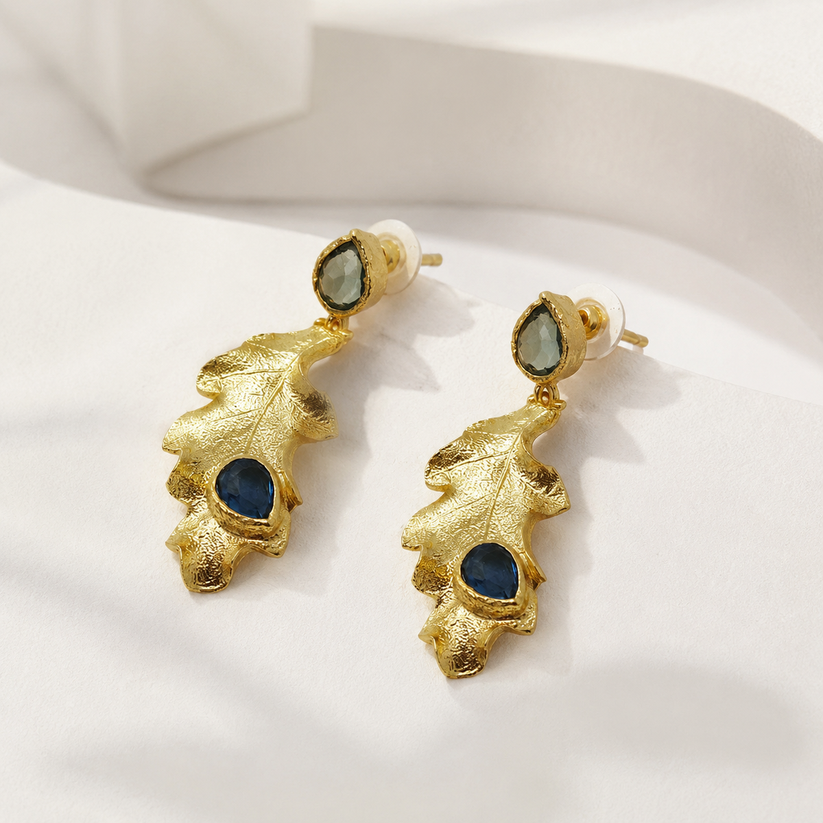 Angle view of textured gold leaf drop earrings with blue stones.