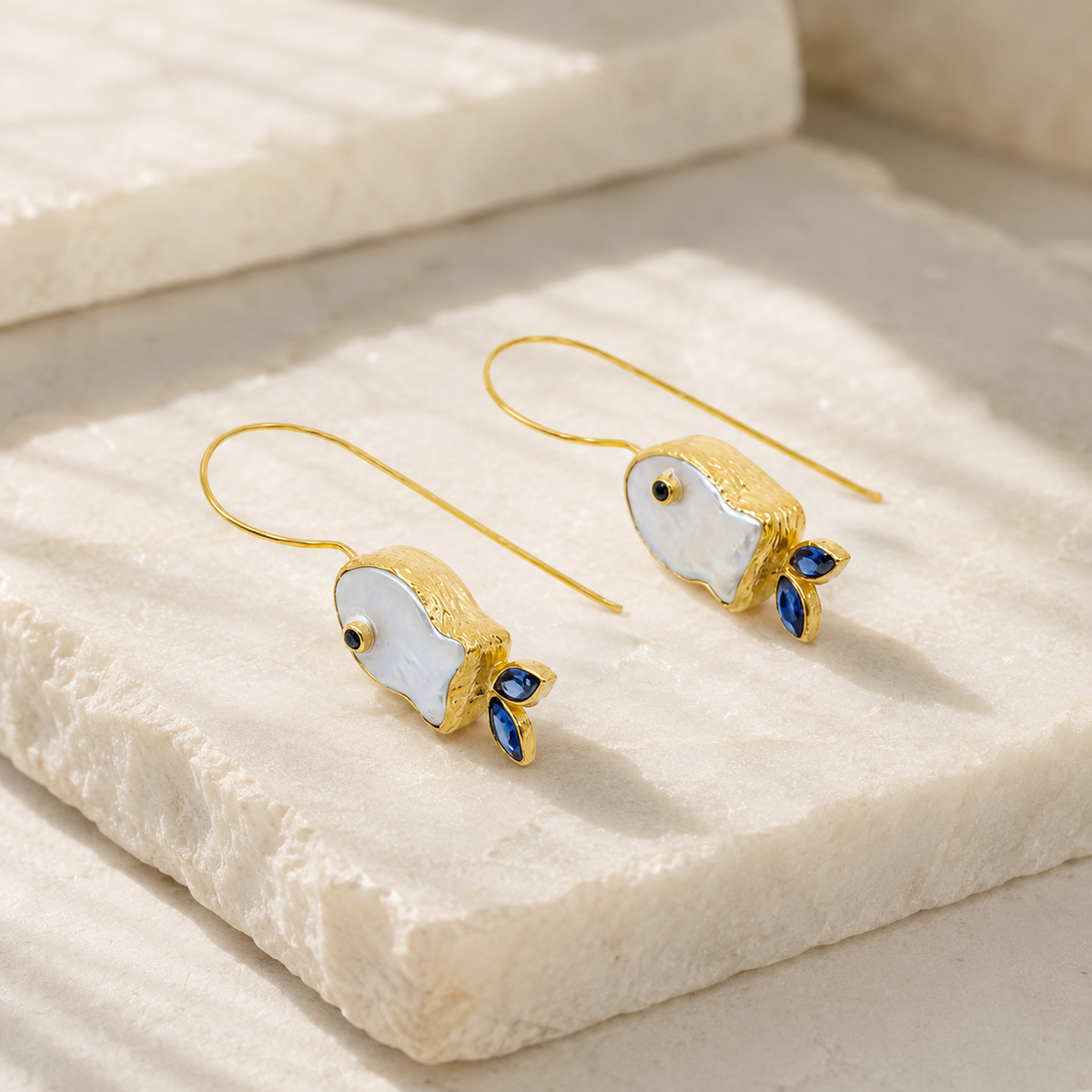 Angle view of pearl-like fish drop earrings with a gold-plated finish.