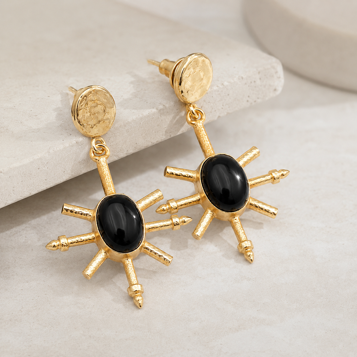 Angle view of gold-plated drop earrings with black onyx centers and spike details.