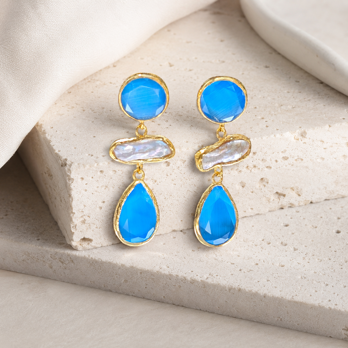 Front view of gold-plated drop earrings with blue faceted stones and a pearl-like center.