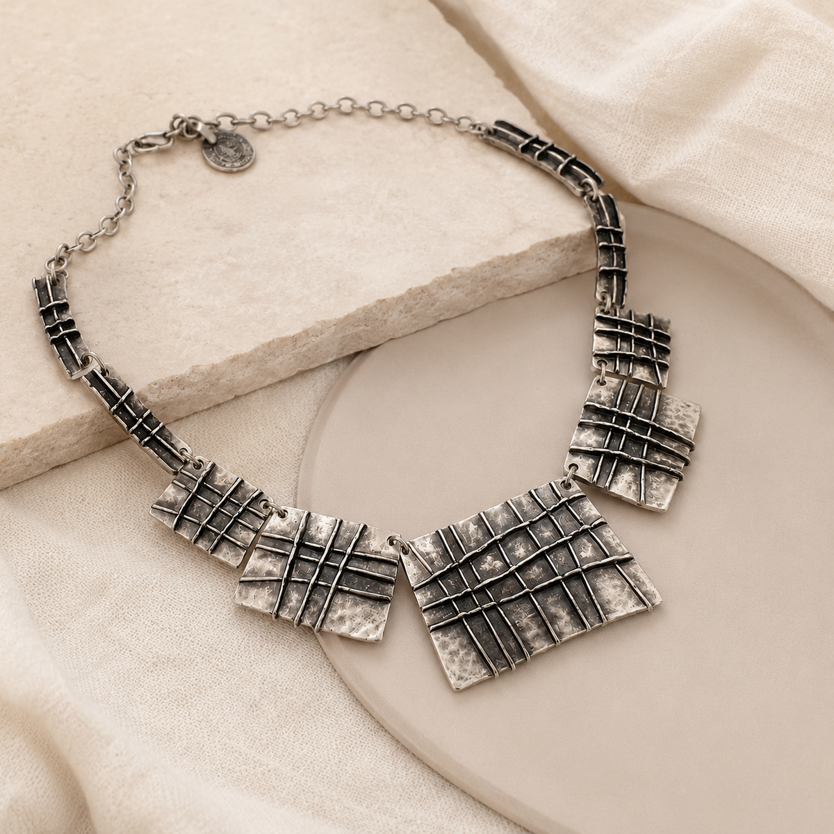 Angled view of a silver-tone necklace with textured plaque pendants.