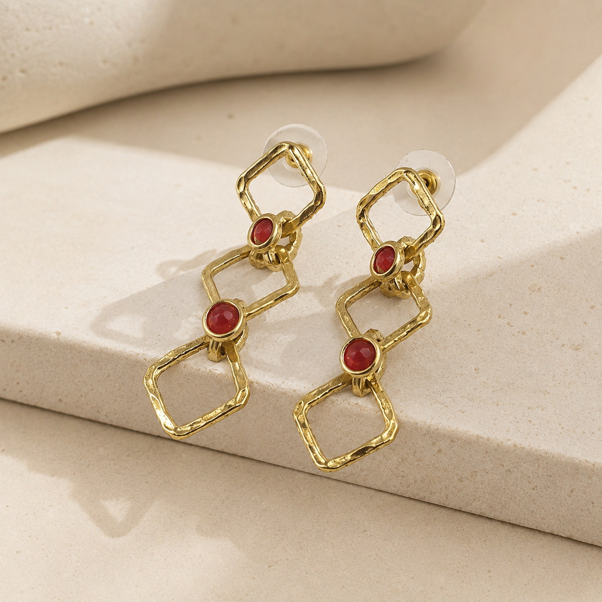 Angle view of gold-tone chain drop earrings with linked geometric shapes and red stone accents.