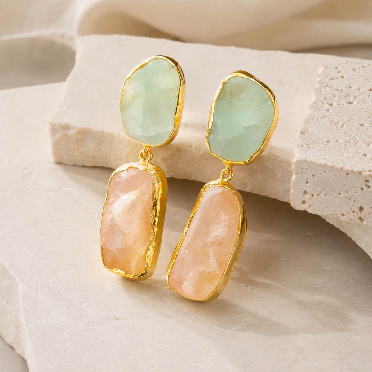 Angled view of gold-plated earrings with rough apatite and rose quartz stones.