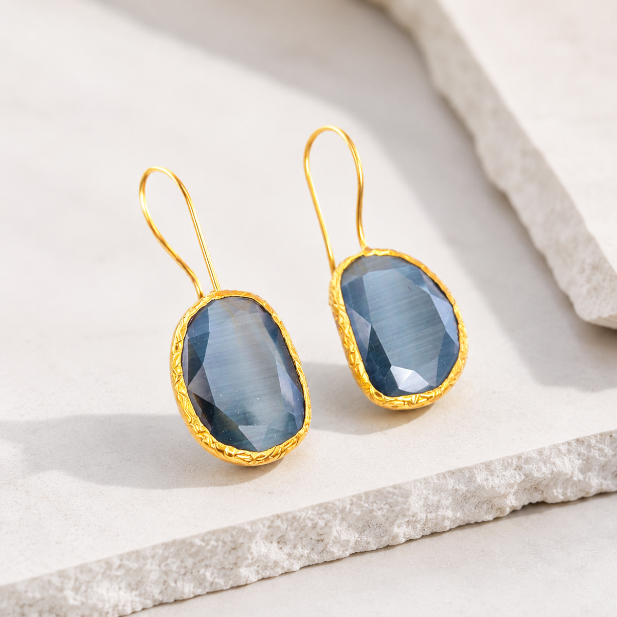Angled view of smoky gray cat eye teardrop earrings with gold-plated frames.