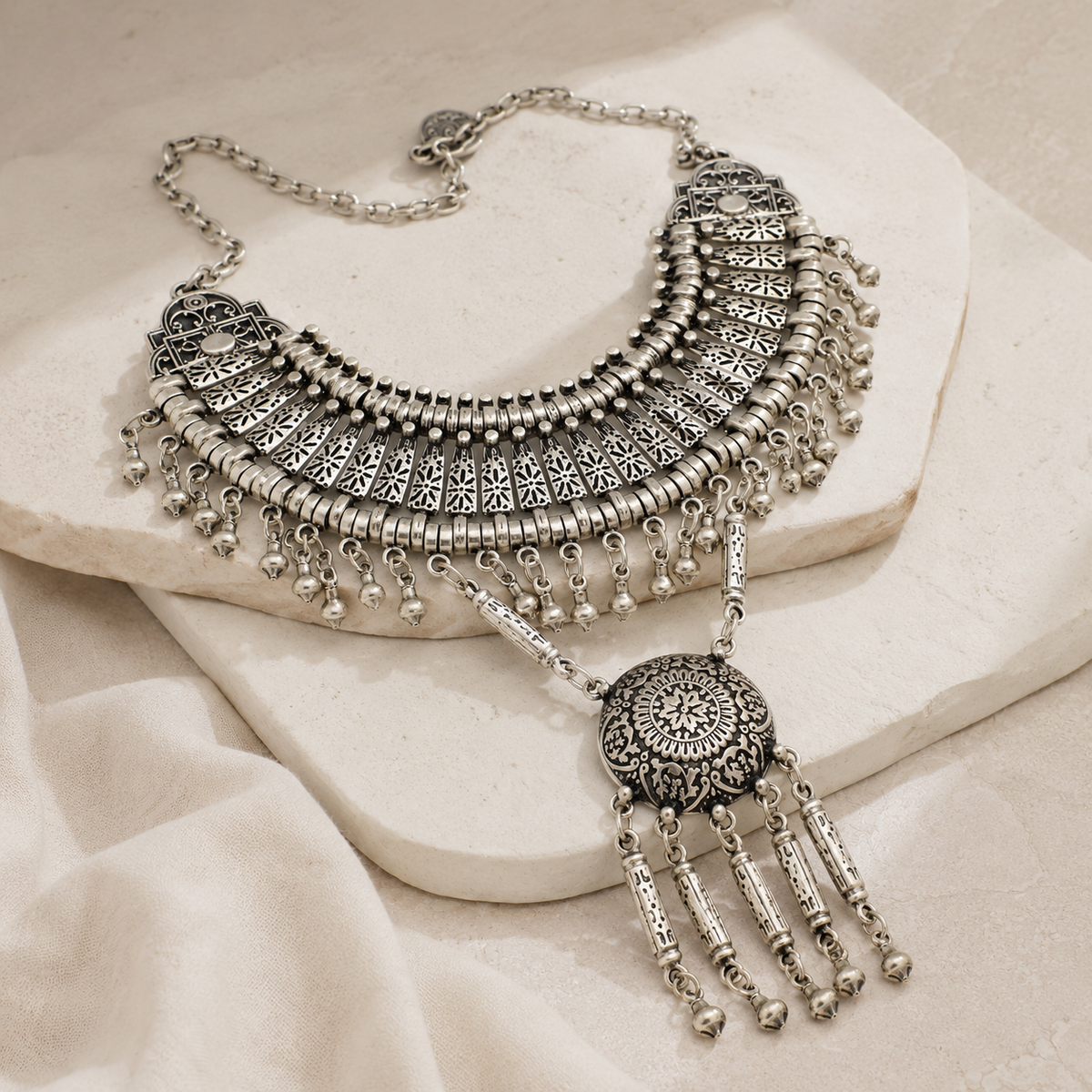 Angled view of a silver-tone boho necklace with layered fan shapes and a round pendant.