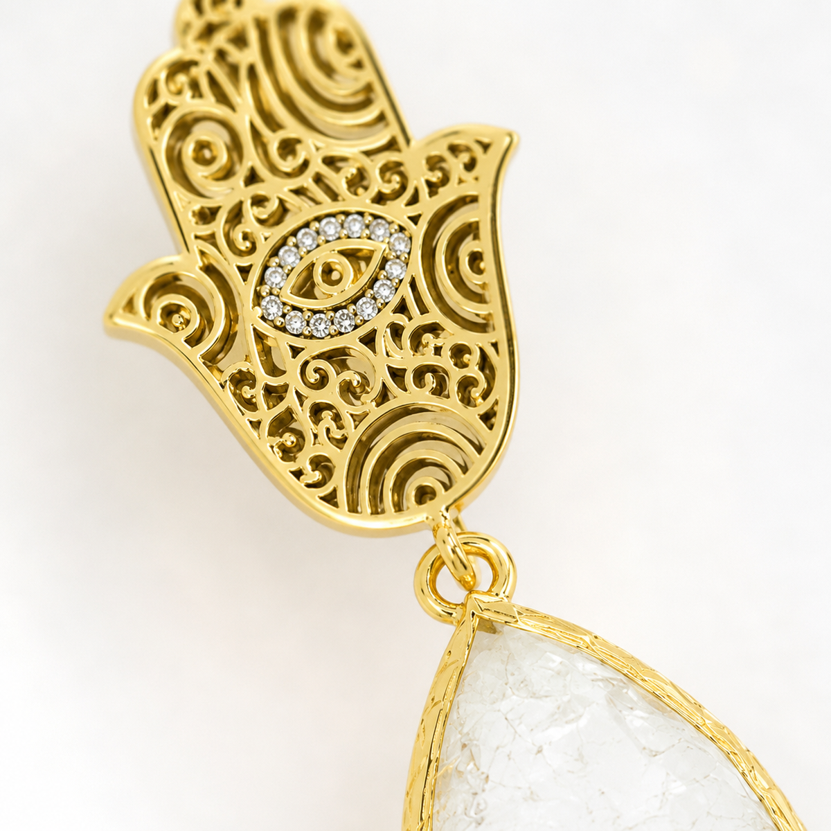 Close view of ornate gold hamsa hand earrings with a white teardrop stone.