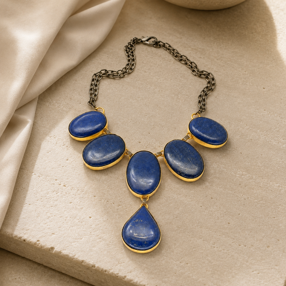 A statement necklace with blue oval stones and a teardrop drop on a white background.