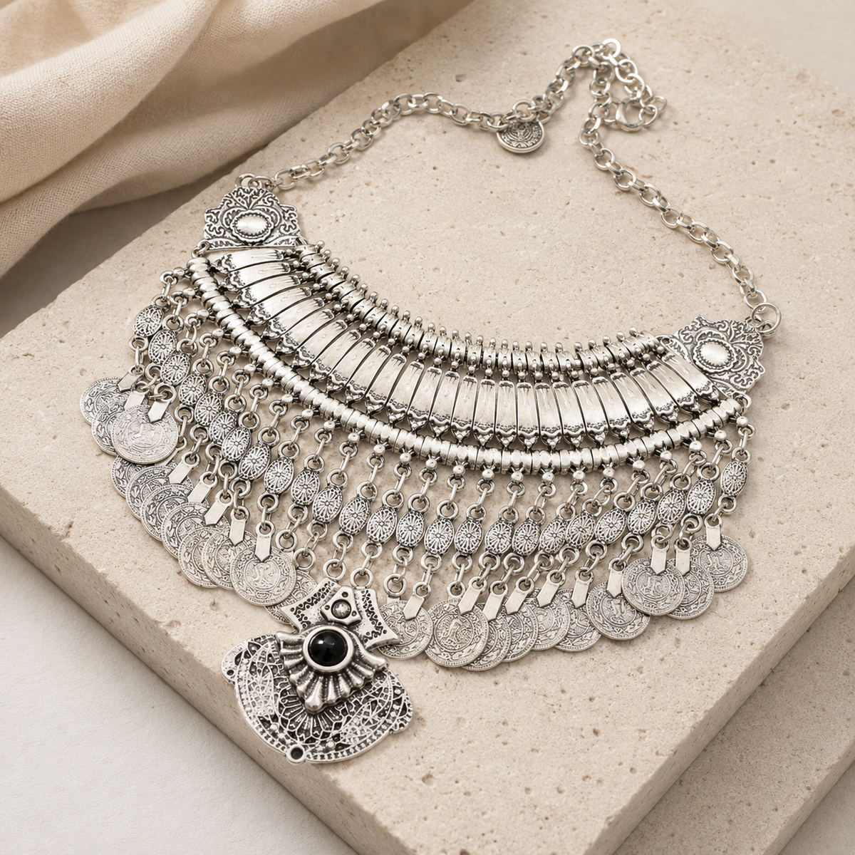 Angled view of a silver-tone coin fringe necklace with a black stone pendant.