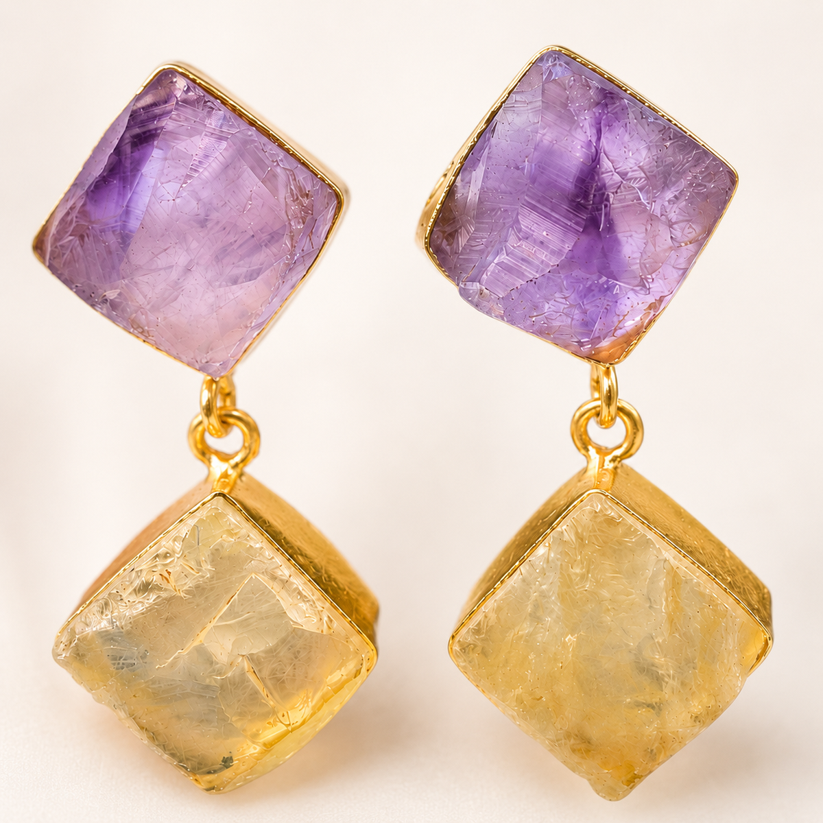Close view of faceted gemstone-style drop earrings in purple and gold tones.