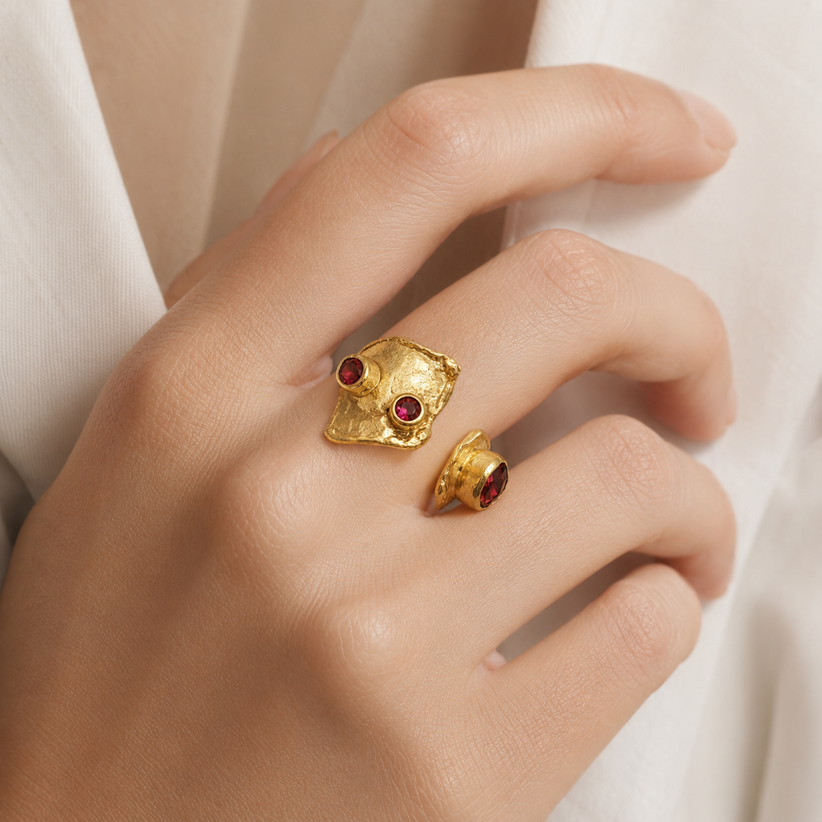 Gold-plated open cuff ring with garnet red stones shown from a front angle.