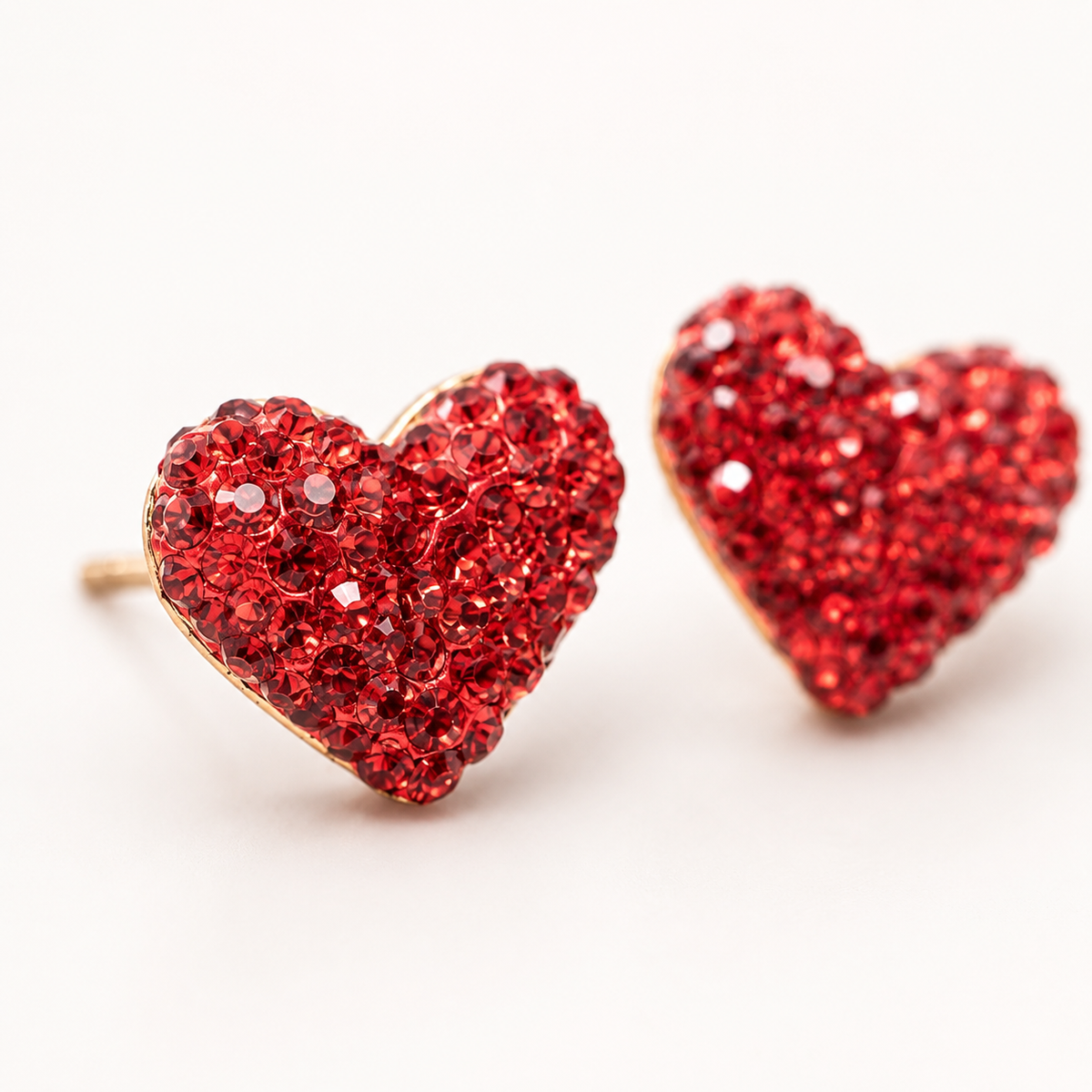 Close view of red crystal heart stud earrings with a sparkling textured surface.
