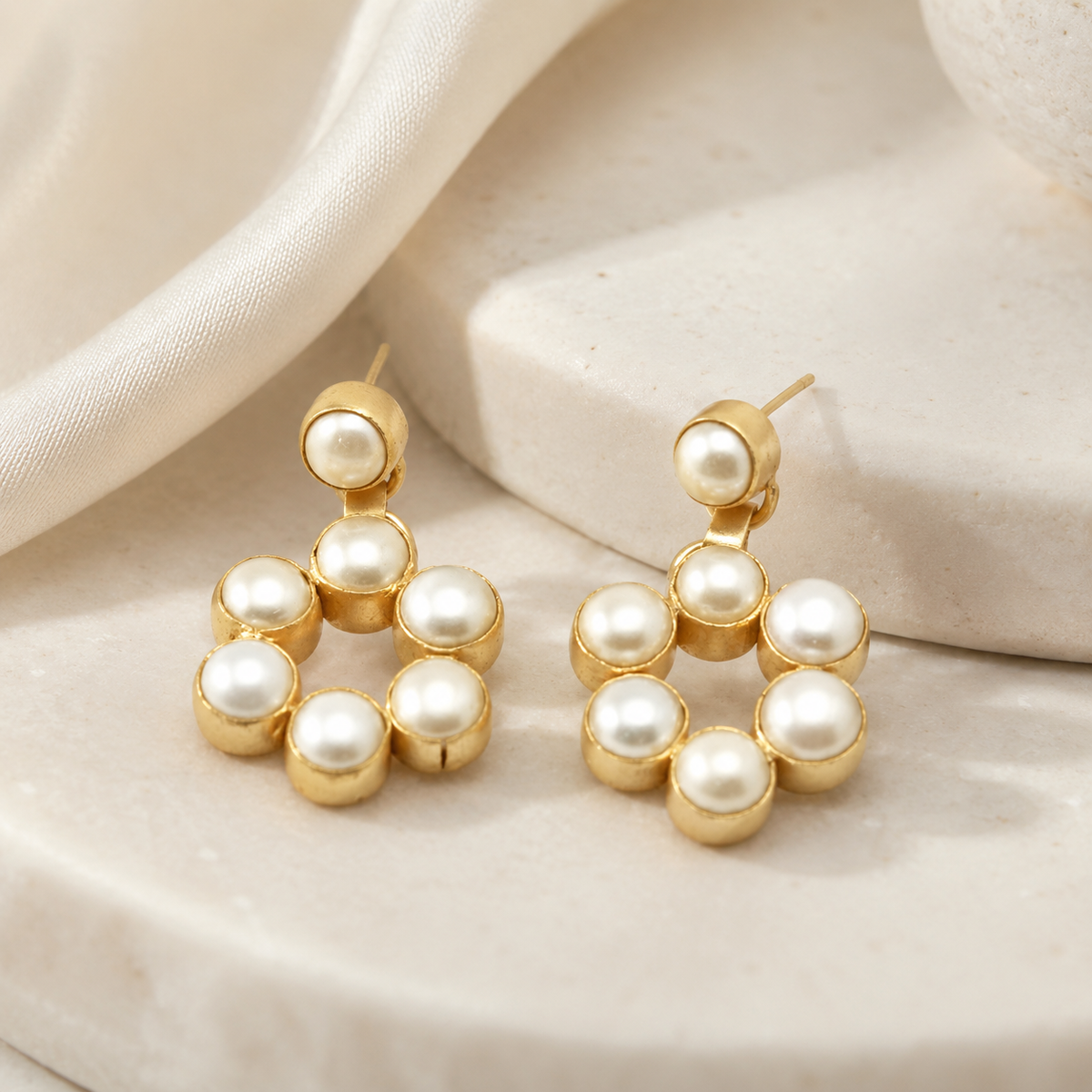 Gold-plated drop earrings with a round pearl design on a white background.