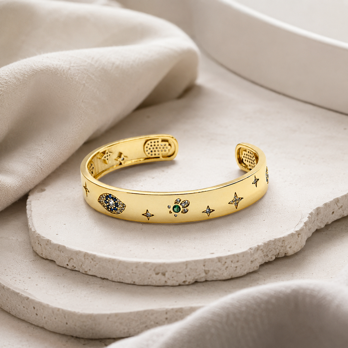 Angle view of a polished gold-tone cuff bracelet with symbolic accents.