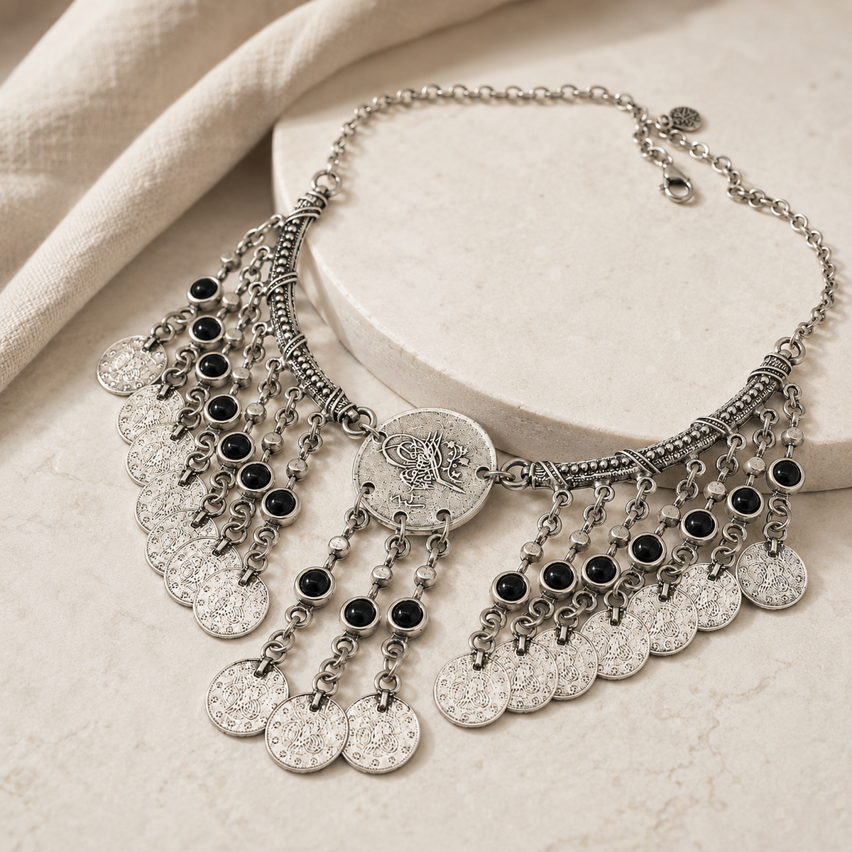 Angled view of an antique silver necklace with black stone accents and coin fringe.