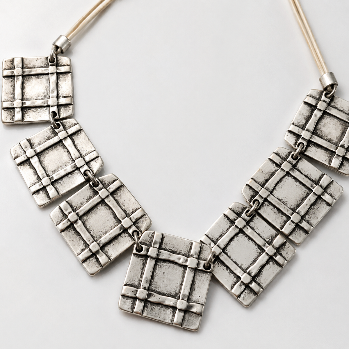 Close view of the square grid pendant details and beige cord.
