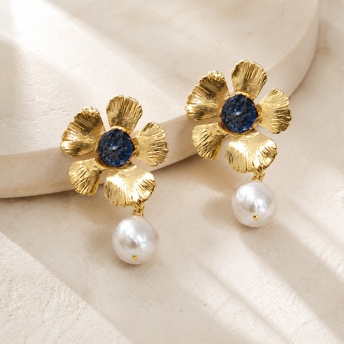 Angle view of gold flower drop earrings with a blue center and pearl drop.