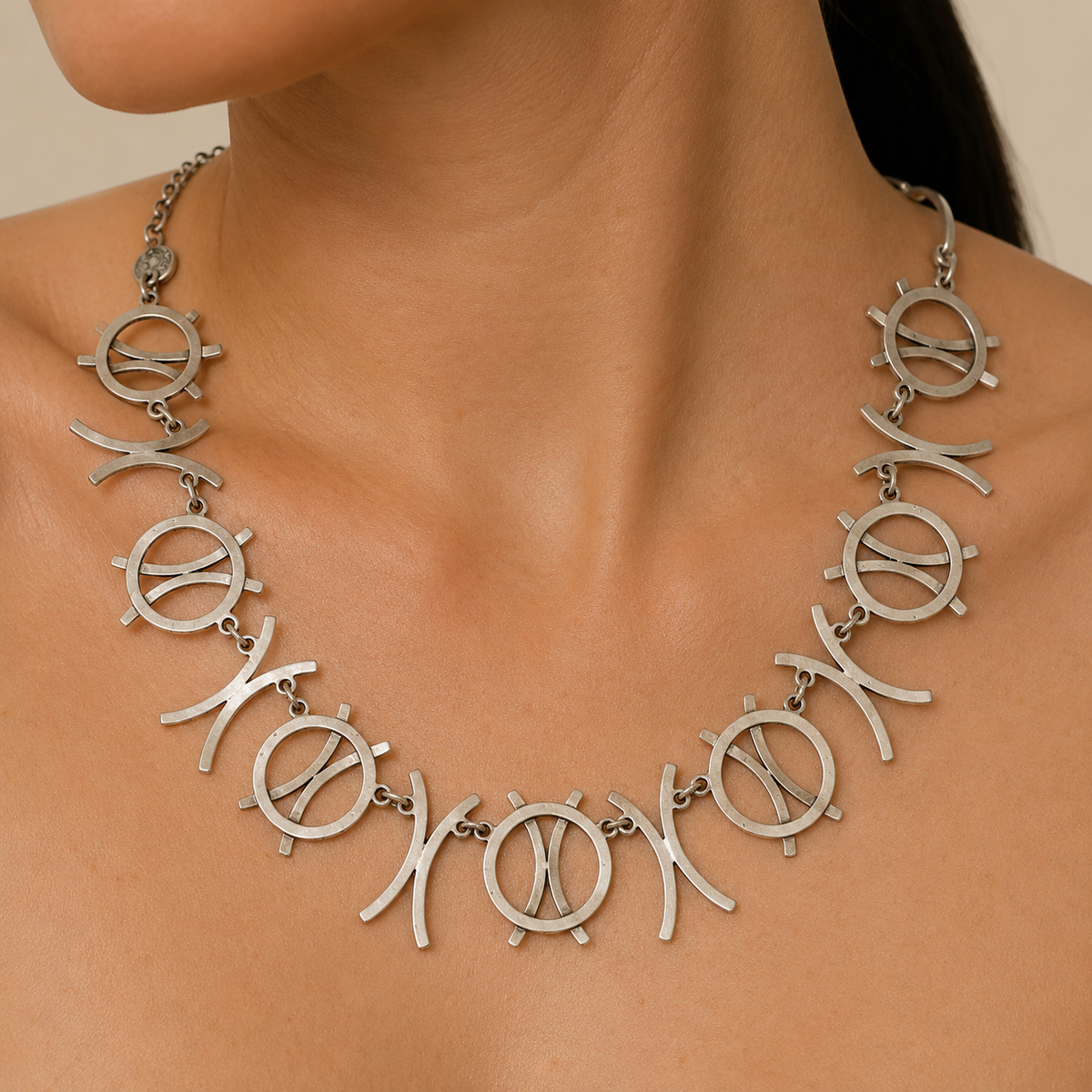 Silver-tone necklace with linked circle symbols and curved shapes on a white background.