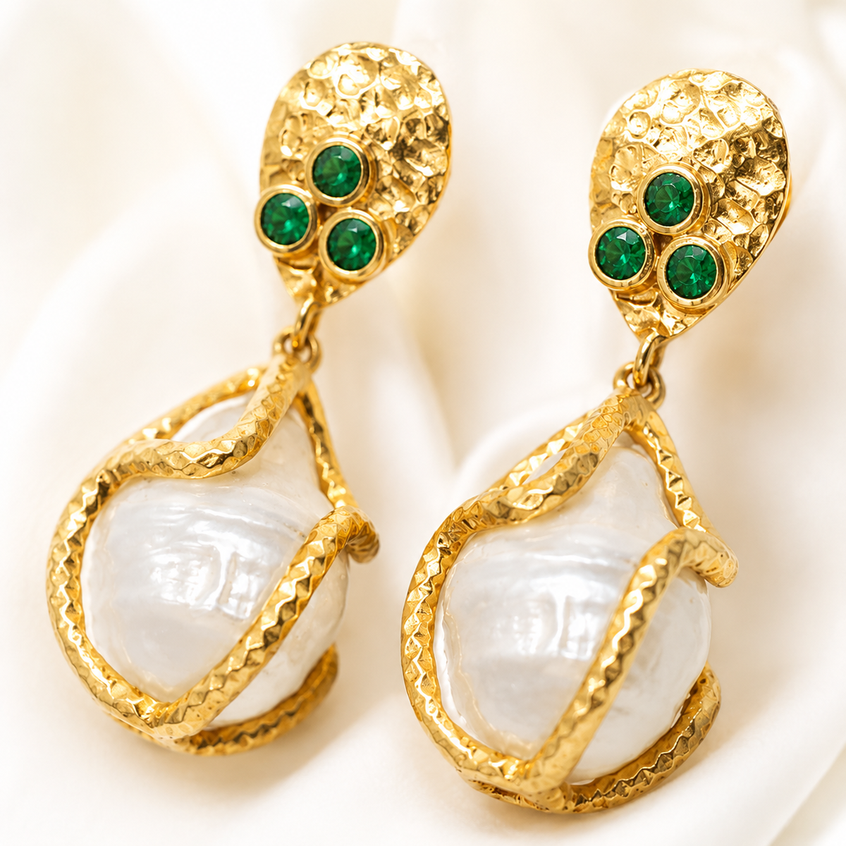 Close view of textured gold-plated earrings with green stones and a pearl-like drop.