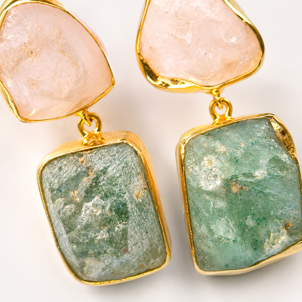 Close view of rough rose quartz and apatite stones framed in gold plating.
