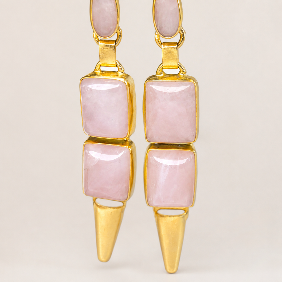 Close view of rose quartz-style stones set in gold-plated geometric drop earrings.