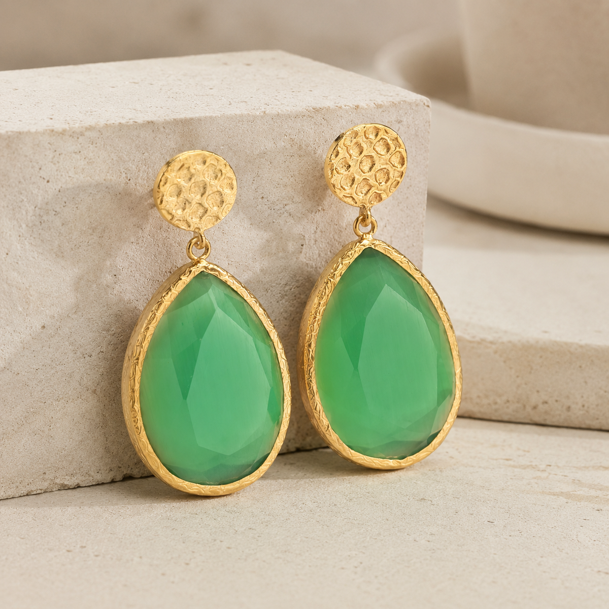 Gold-plated teardrop earrings shown at a slight angle with textured round studs and green faceted drops.