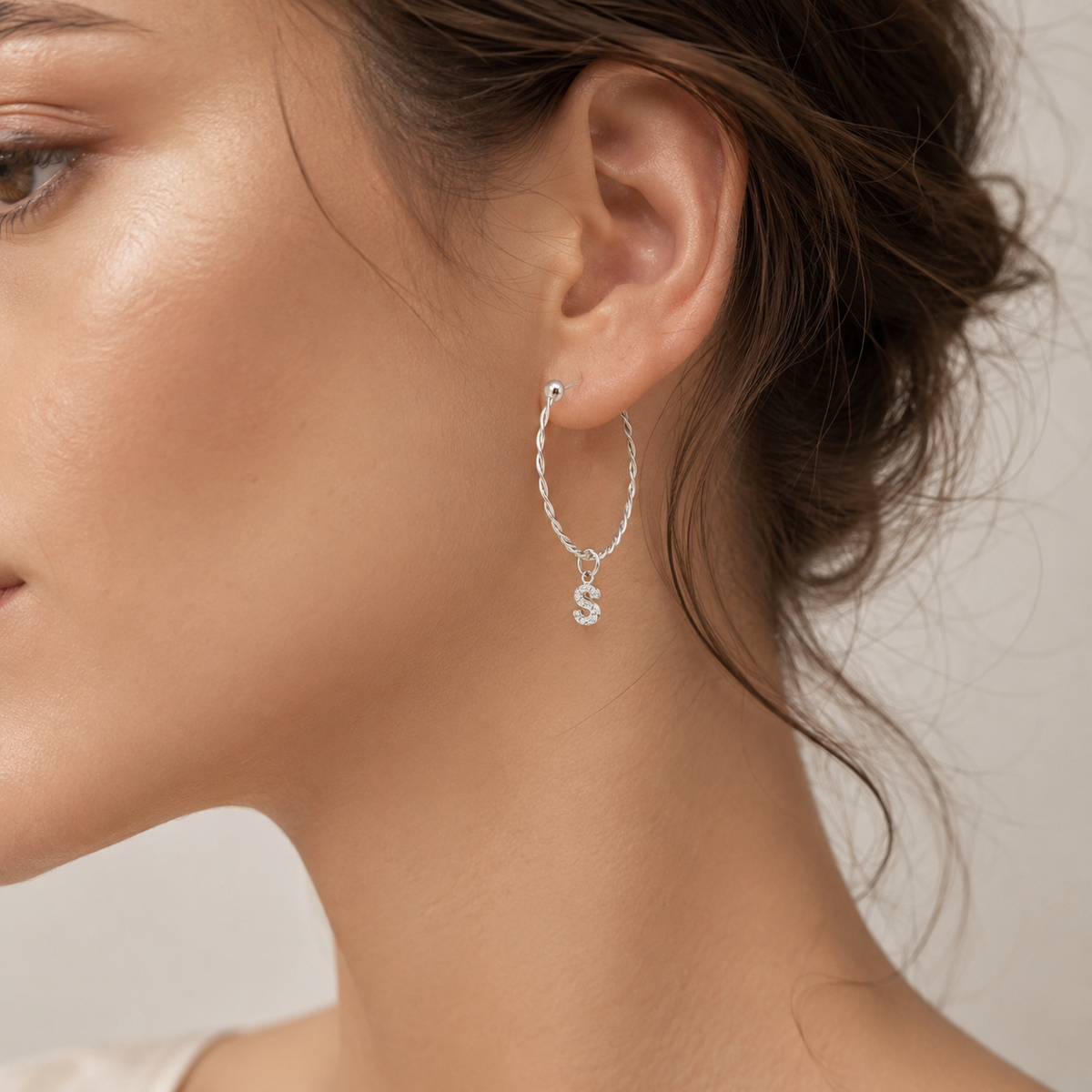 Twisted hoop earrings shown from a side angle with an initial charm.