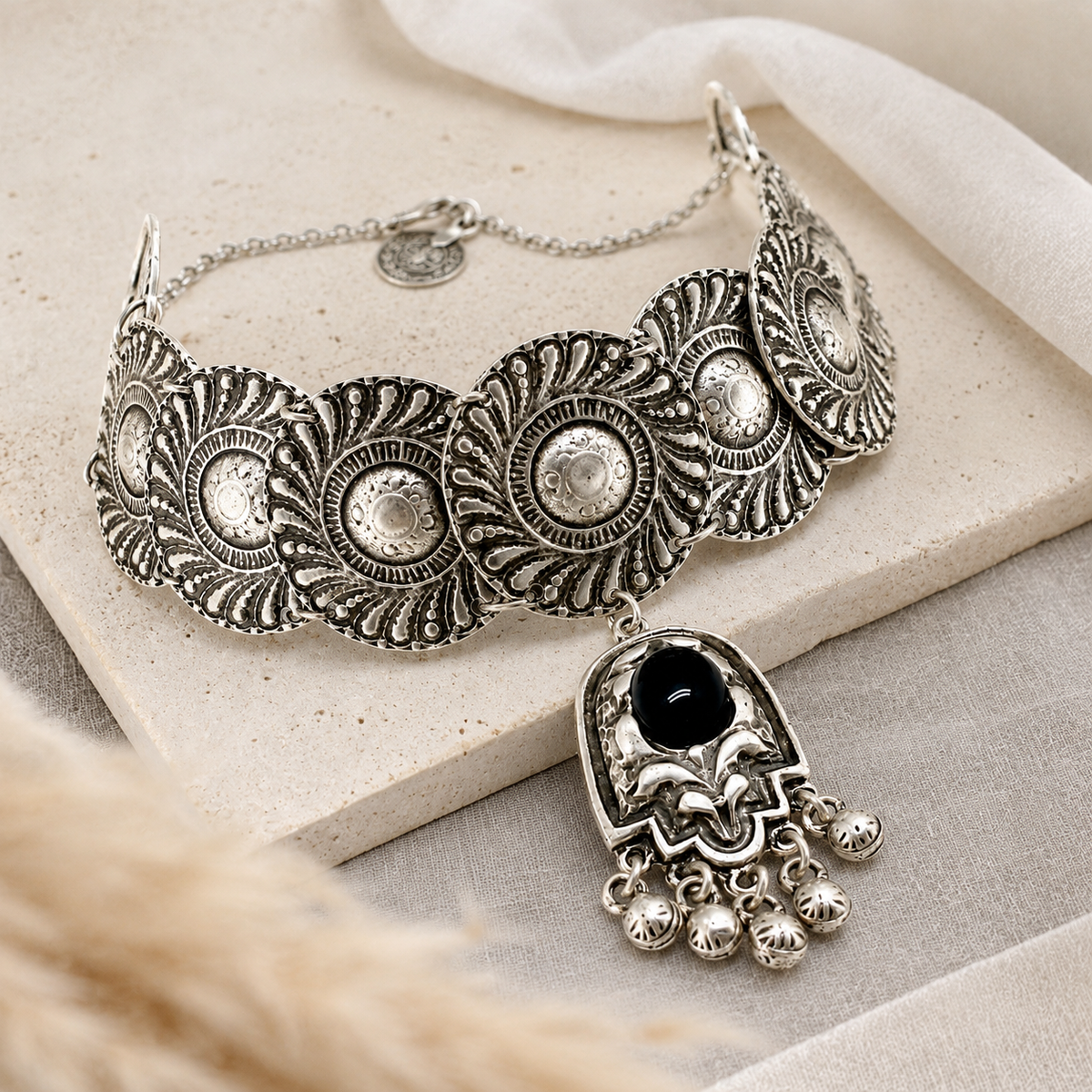 Silver-tone statement choker necklace with ornate disc links and a black stone drop.