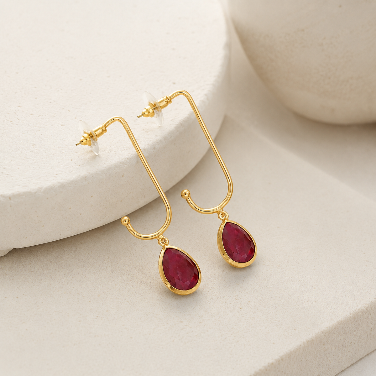 Angled view of gold-plated open drop earrings with green stone pendants.