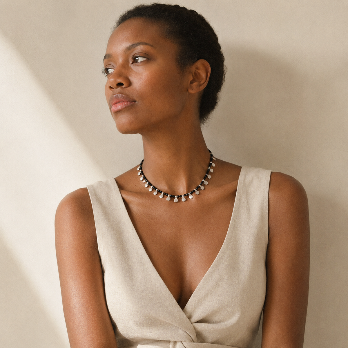Black bead necklace with silver disc accents shown in a campaign-style product image.