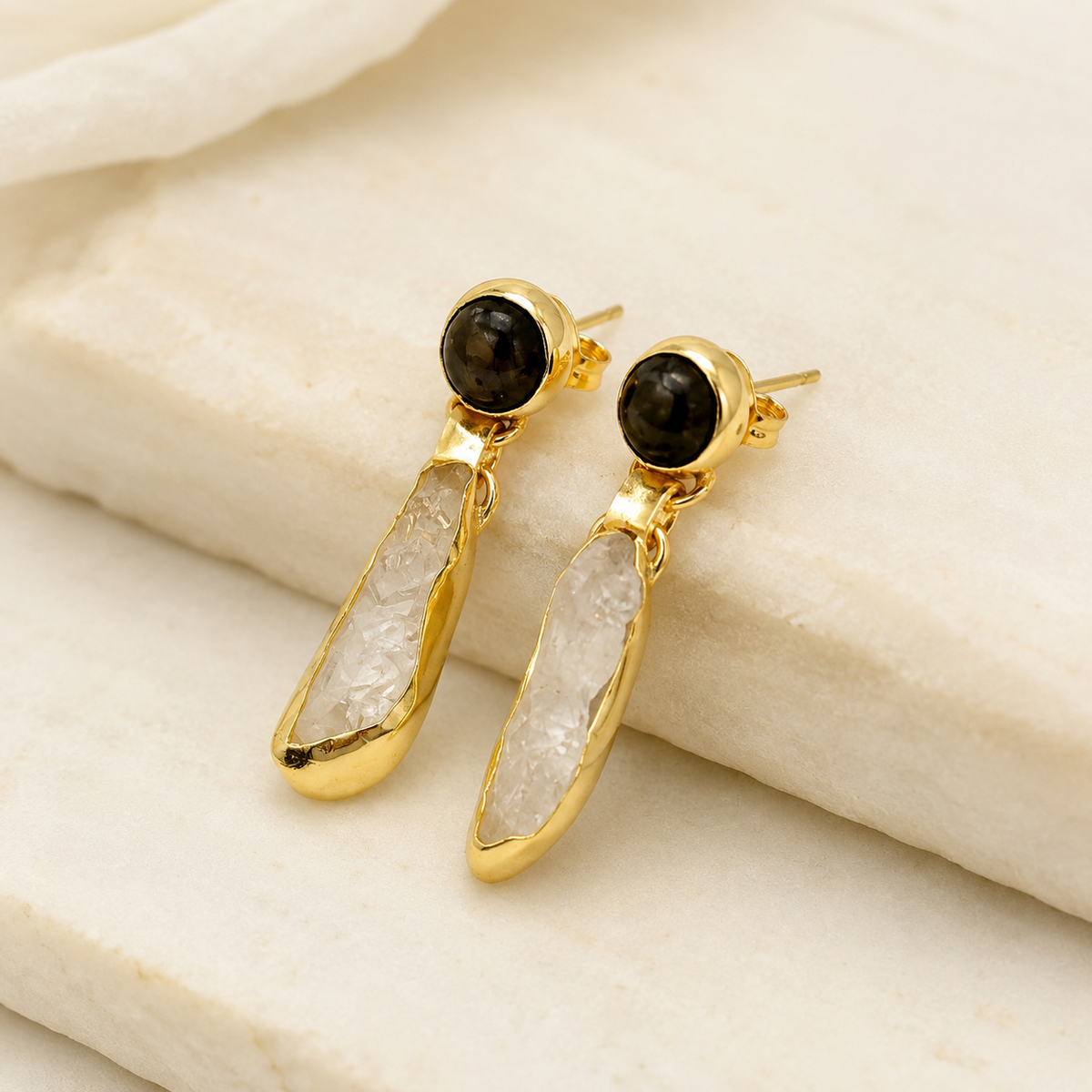 Angle view of gold plated drop earrings with smoky quartz and clear quartz details.