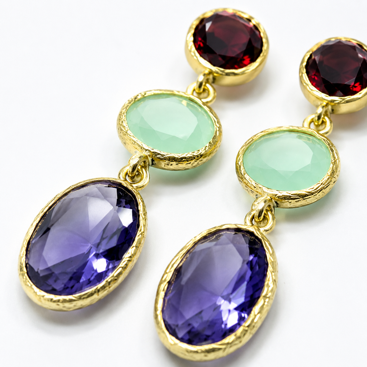 Close view of gold-plated drop earrings with faceted red, green, and blue stones.