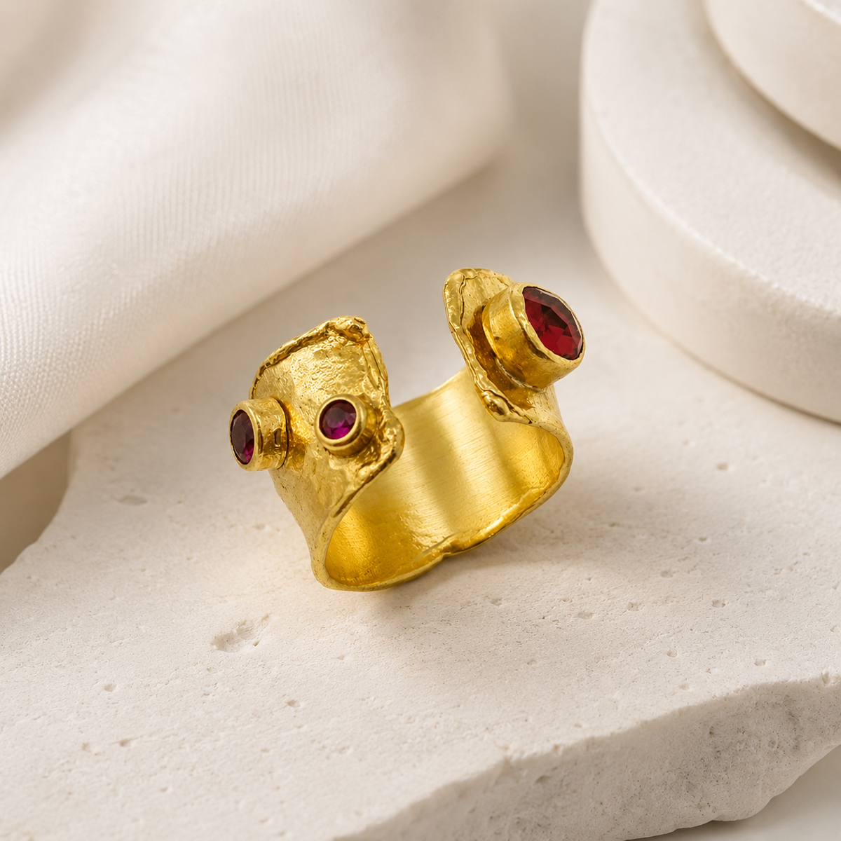 Gold-plated open cuff ring with a sculptural shape and garnet red accents.
