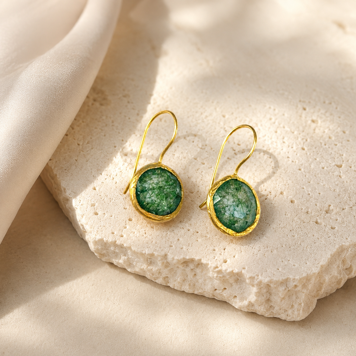 Pair of gold-plated drop earrings with green stones on a white background.