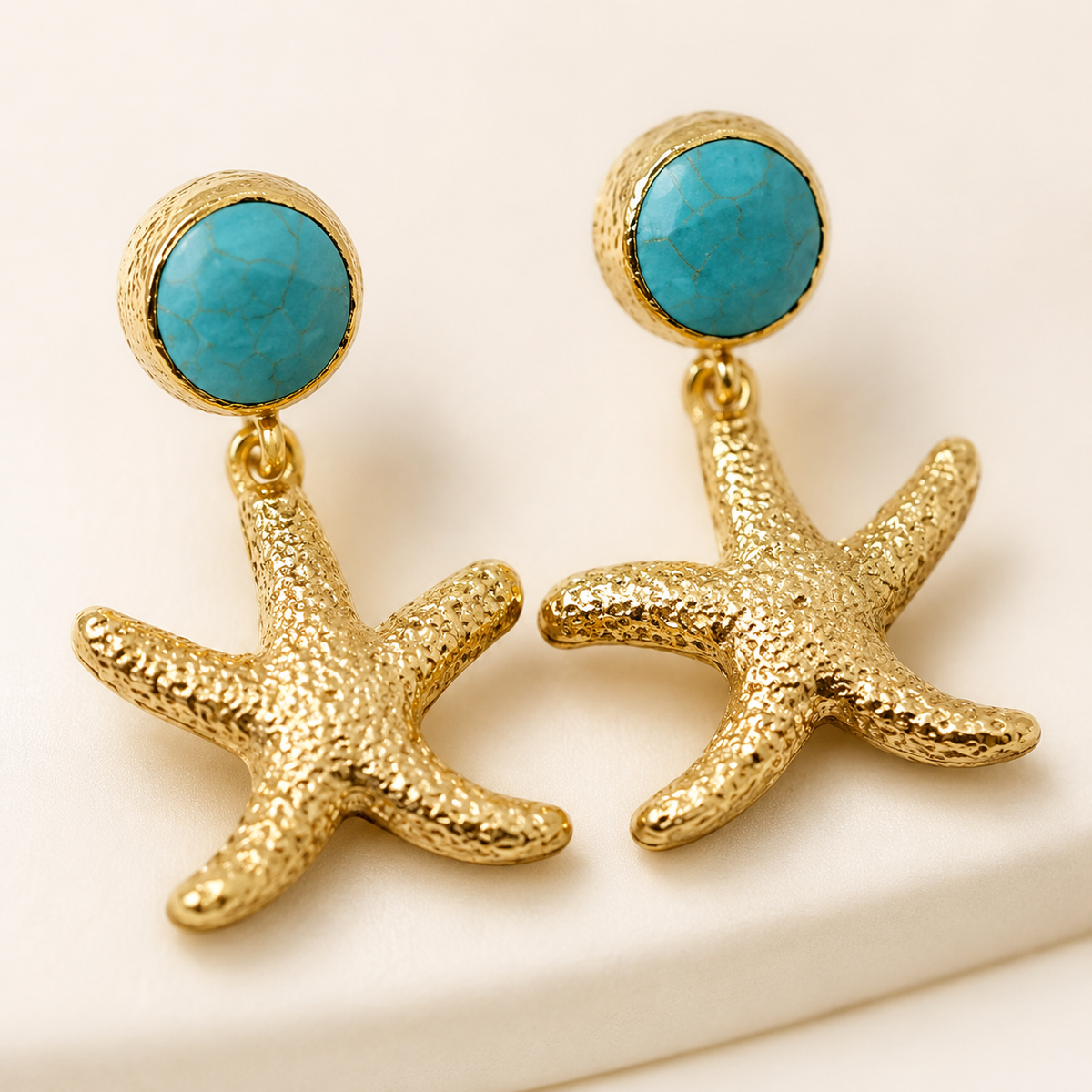 Close view of textured gold starfish earrings with turquoise accents.