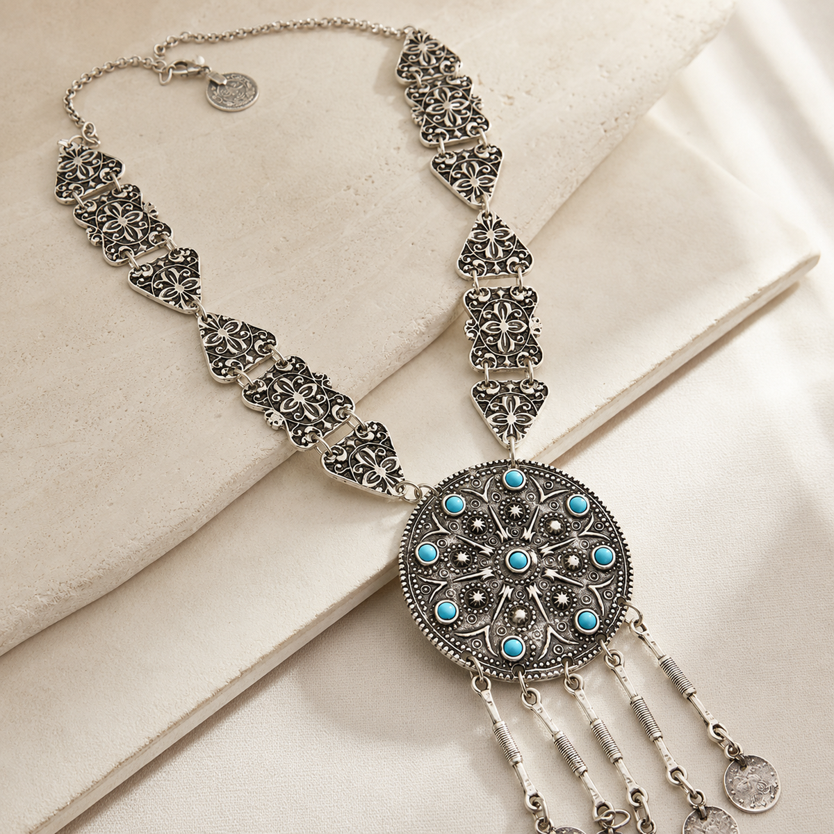 Angled view of a silver-tone necklace with ornate links and turquoise details.