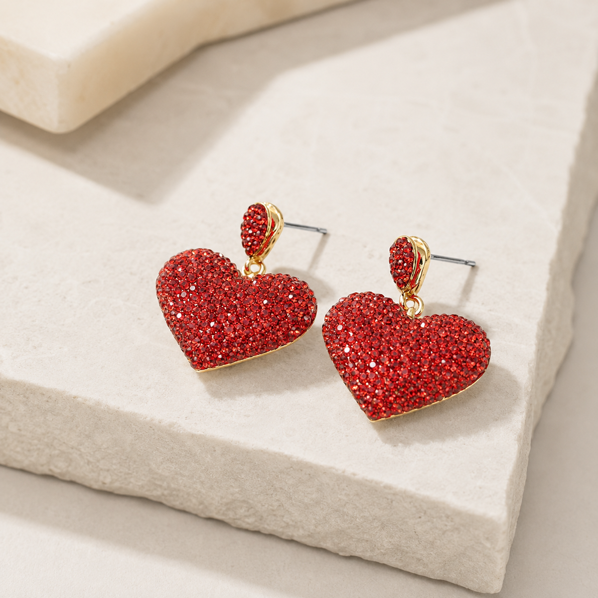 Angled view of red crystal heart stud earrings with a gold-plated finish.